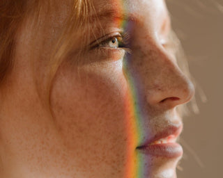Ein weibliches Gesicht mit Sommersprossen und gebrochenem Licht in Regenbogenfarben