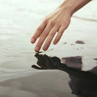 Die Hand einer Person greift in ein Gewässer.