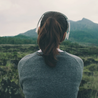 Eine Frau hört Musik auf einem Feld mit Bergen im Hintergrund.