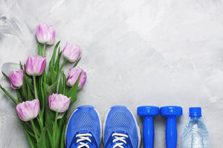 Ein Strauß rosafarbener Tulpen, blaue Sportschuhe, blaue Sportgewichte und eine Flasche Wasser