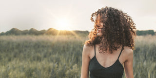 Eine Frau mit lockigem Haar steht bei Sonnenuntergang auf einem Feld.