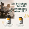 Eine Frau und ein Kind sitzen bei Sonnenuntergang am Strand über Bildern des Vitamin C - Familiensets von Nature Love, mit deutschem Text, der die Unterstützung des Immunsystems und der geistigen Gesundheit hervorhebt.