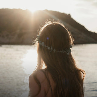Ein Mädchen mit langen Haaren steht bei Sonnenuntergang am Wasser.