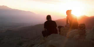 Eine Gruppe von Menschen sitzt auf einem Felsen und blickt auf den Sonnenuntergang.